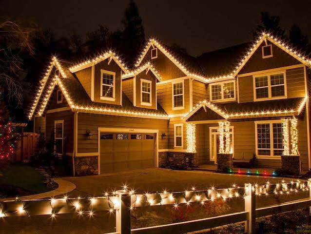 A home decorated with warm white Christmas lights along the roofline and driveway at night
