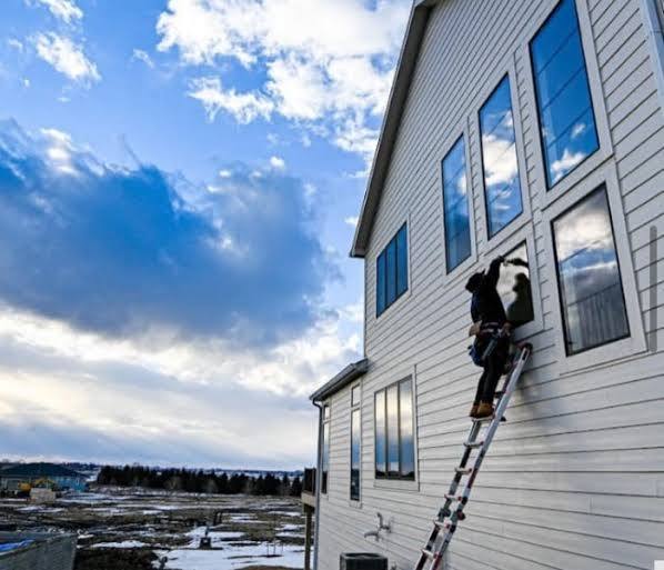 Ladder work on upper windows of a white sided home
