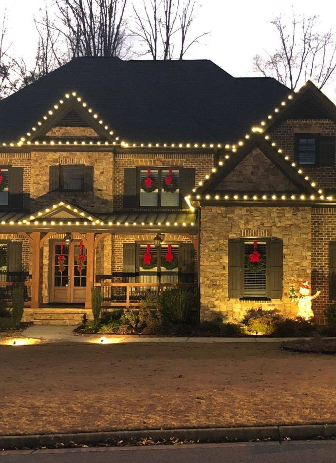 Warm white roofline lighting and wreaths on a two-story brick home
